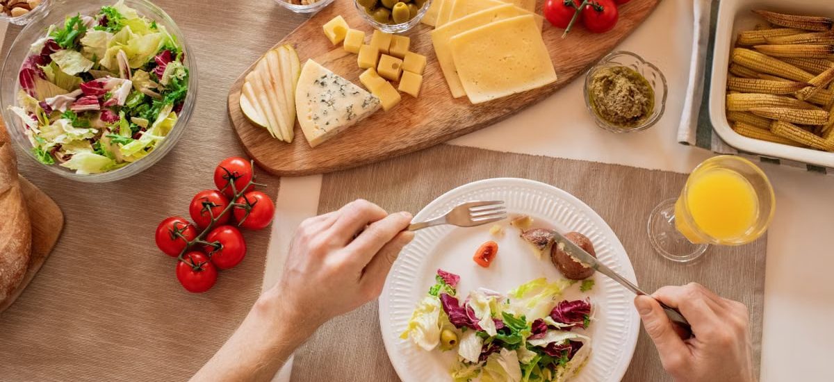 Overhead view of a cheese platter with fresh salad and juice, perfect for a gourmet lunch setting.