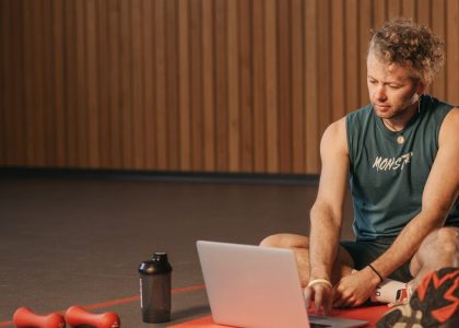 Man sitting on exercise mat with laptop, surrounded by dumbbells, creates a unique fitness workspace.